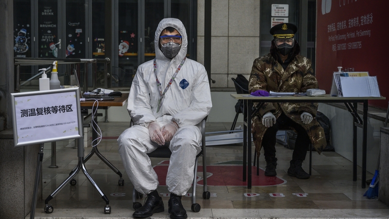 A Chinese guard wears a protective mask and suit as he waits to check temperatures and register people entering a building in a commercial area