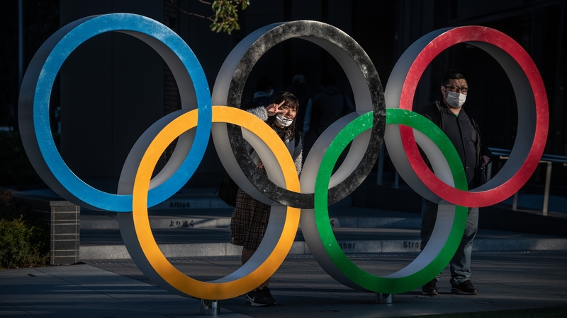 People wearing masks pose for photos next to the Olympic rings in Tokyo earlier today