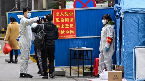 A man wearing a protective suit takes the temperature in a neighborhood in Wuhan