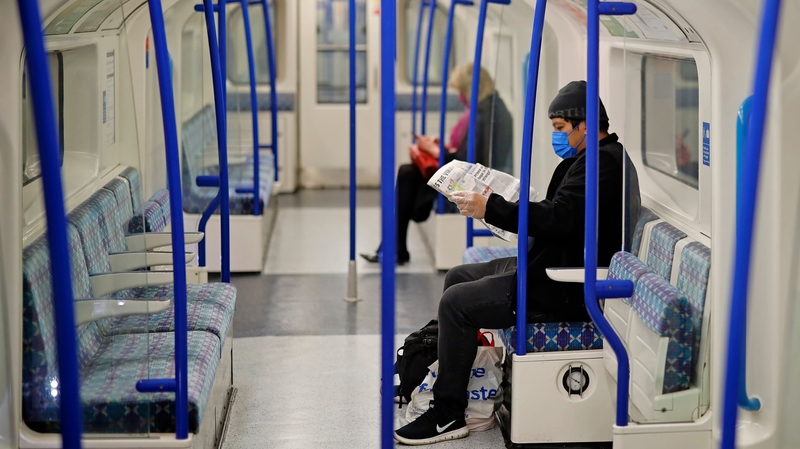 Two people, one wearing a face mask as a precautionary measure, sit on an empty London underground tube carriage