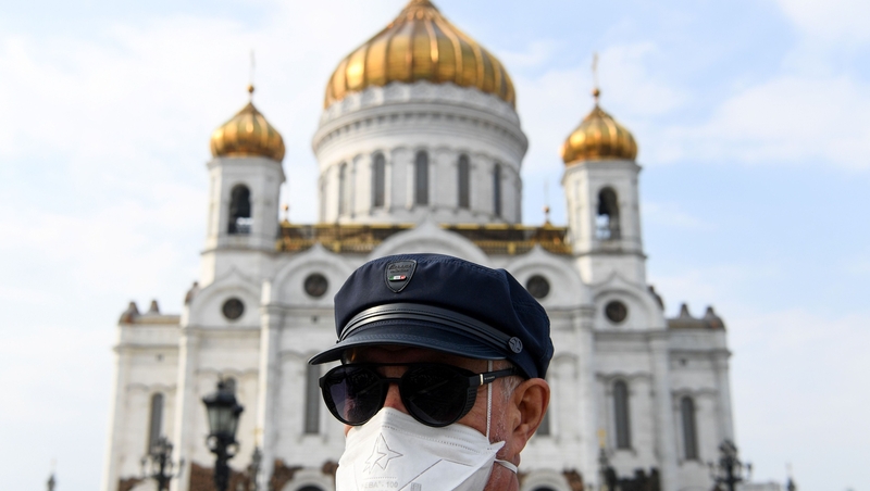A person wearing a protective face mask stands in front of the Christ the Savior Cathedral in Moscow