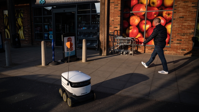A man walks past a robot as it makes a home delivery in Milton Keynes