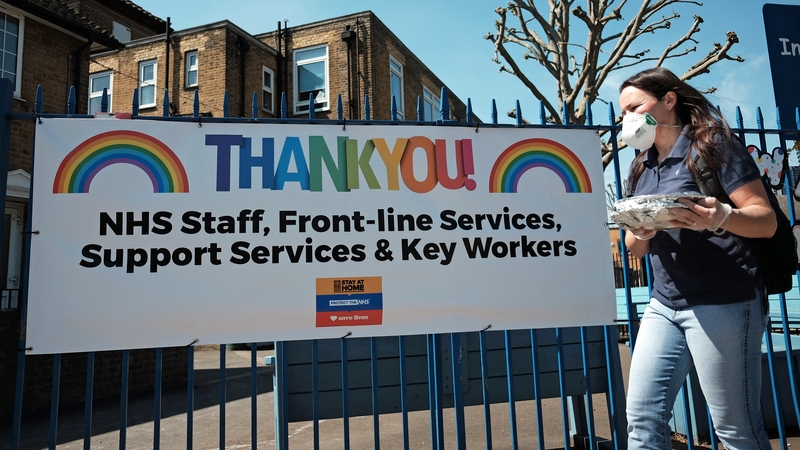 A woman wearing a face mask walking past a 'Thank You' to NHS sign in London