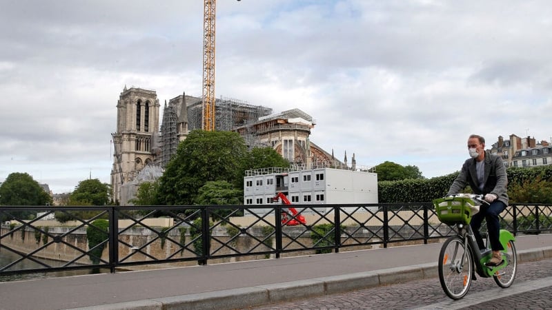 A man wearing a protective face mask rides his bike next to Notre-Dame Cathedral in Paris
