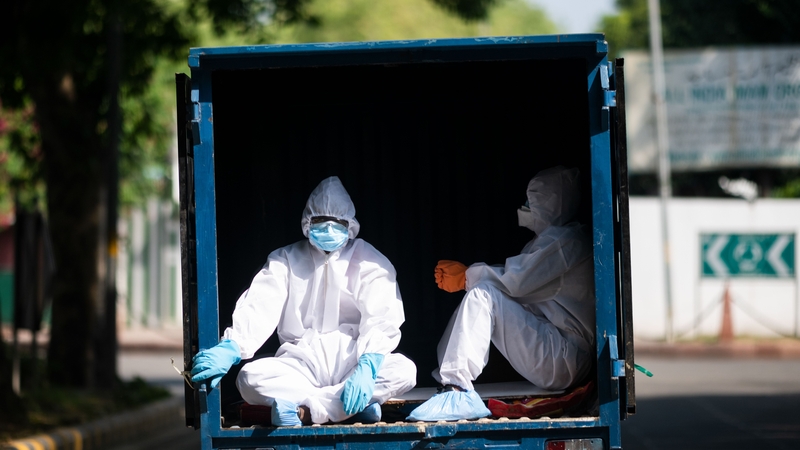Men wearing PPE ride in the back of a vehicle in New Delhi in India