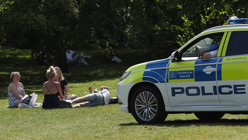Police officers in a patrol car move sunbathers on in Greenwich Park, London
