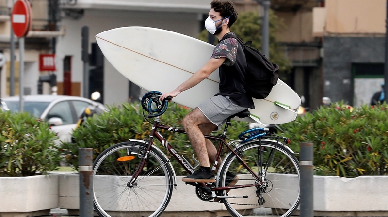 A surfer wearing a protective face mask on his way to the beach in Valencia, Spain
