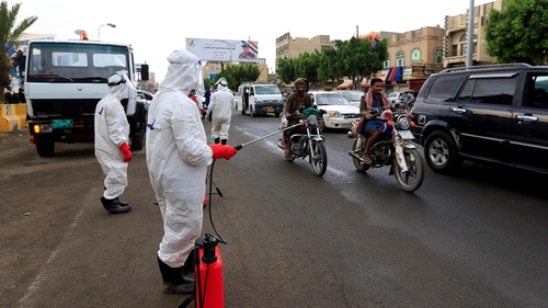 Yemeni workers wearing a protective outfits spray disinfectant on passing cars and motorcycles in Sanaa