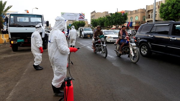 Yemeni workers wearing a protective outfits spray disinfectant on passing cars and motorcycles in Sanaa