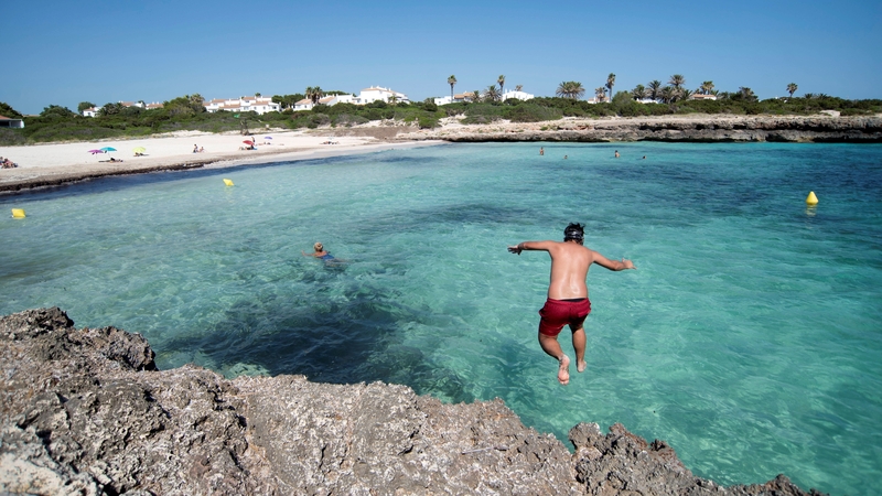 A man jumps into the sea at an almost empty beach in Menorca, Spain