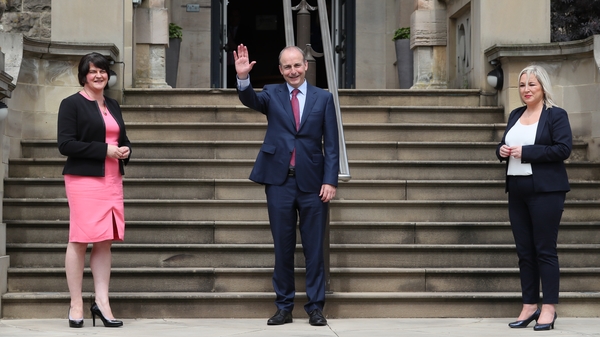 Micheál Martin waving to reporters alongside Arlene Foster (left) and Michelle O'Neill at Stormont Castle in Belfast today