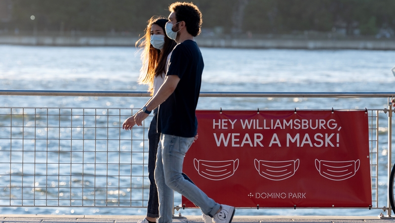 People wearing masks walk past a 'hey Williamsburg, wear a mask' sign in Brooklyn, New York