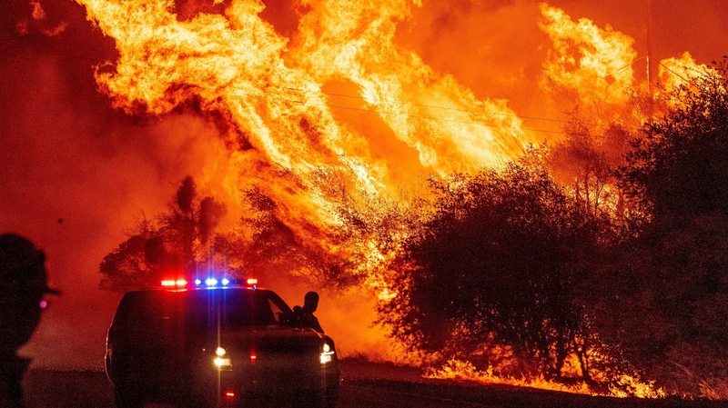 A law enforcement officer watches flames launch into the air as fire continues to spread during the Bear fire in Oroville, California today