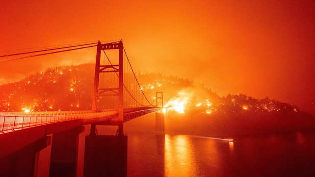 A boat motors by as the Bidwell Bar Bridge is surrounded by fire in Lake Oroville during the Bear fire in Oroville
