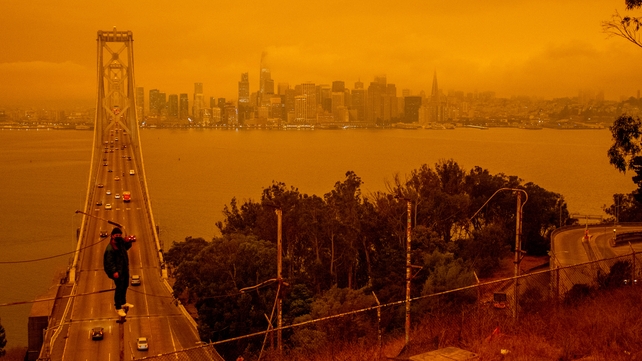 Jose Castillo has his photo taken with the Bay Bridge and the San Francisco skyline in the background by his friend Laito Miyake, both of San Francisco, as smoky skies from the northern California wildfires casts an orange and yellow color in San Francisc