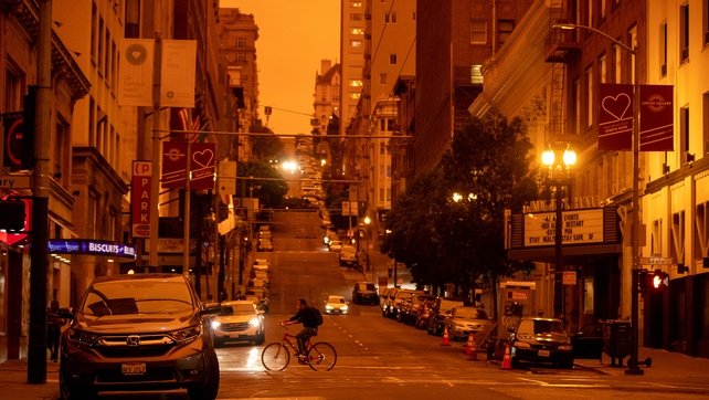 A person rides a bike on Geary and Mason streets as smoky skies from the northern California wildfires casts a reddish color around noon in San Francisco