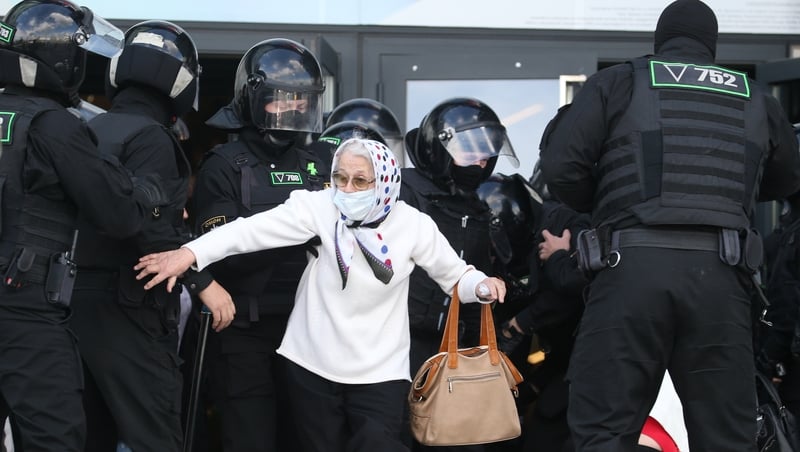 An elderly woman is arrested by police as thousands of people take to the streets of Minsk