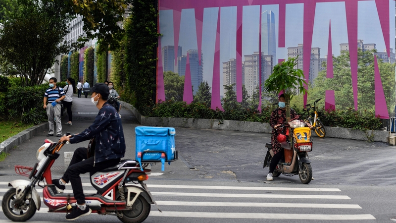 People, wearing faces masks, are seen past a billboard promoting their city in Wuhan