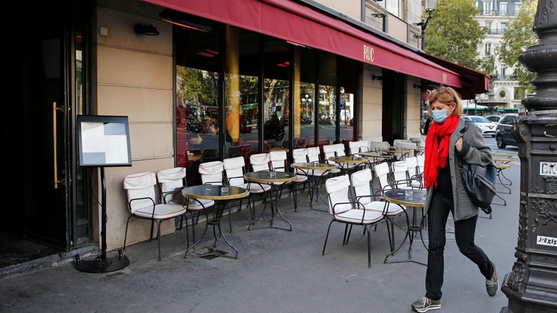 A woman walks past an empty cafe terrace next to the Rue de Rivoli in Paris