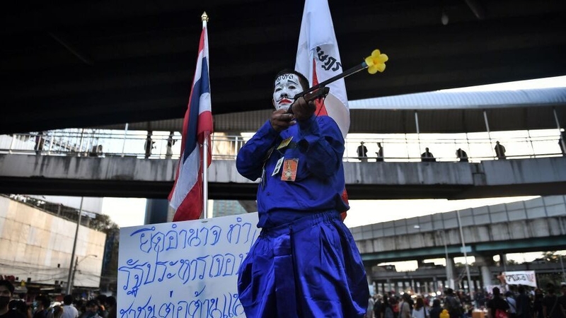 A pro-democracy protester poses with a gun with a flower in the barrel during the Bangkok rally