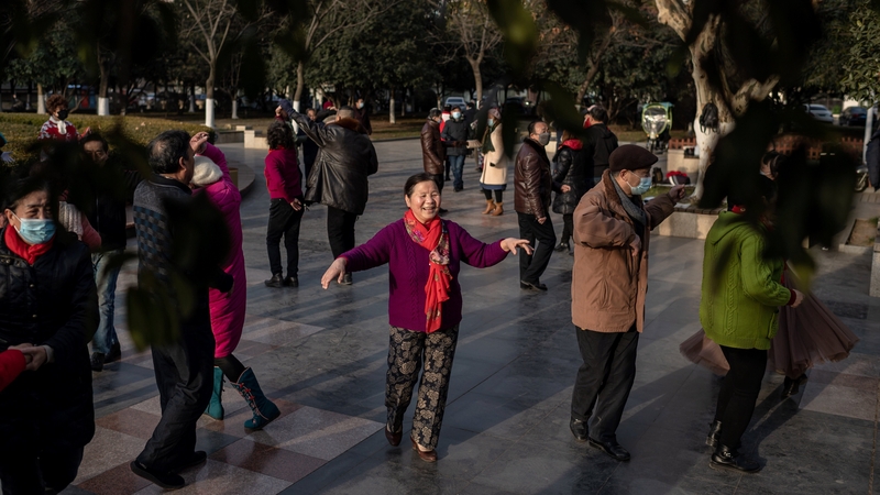 People dance in a busy park next to the Yangtze river