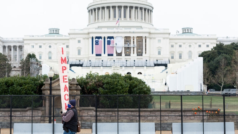 Workers hang flags on the US Capitol for the inauguration as a man carrying an impeach sign protests nearby