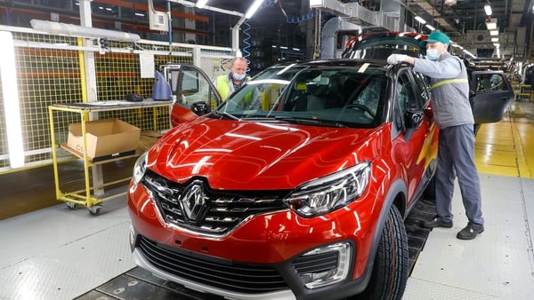 a worker standing next to a red car in Renault factory