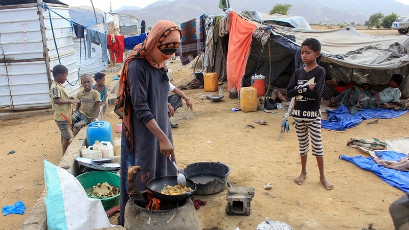 Children play near tents as a woman cooks outdoors at a makeshift camp for the displaced