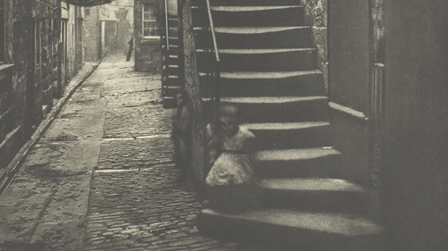 A child sits on the steps of a tenement building in Glasgow in the mid 19th century.