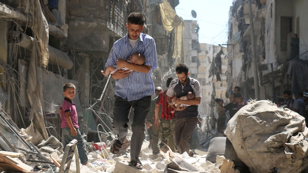 Syrian men carrying babies make their way through the rubble after an air strike in Aleppo in September 2016