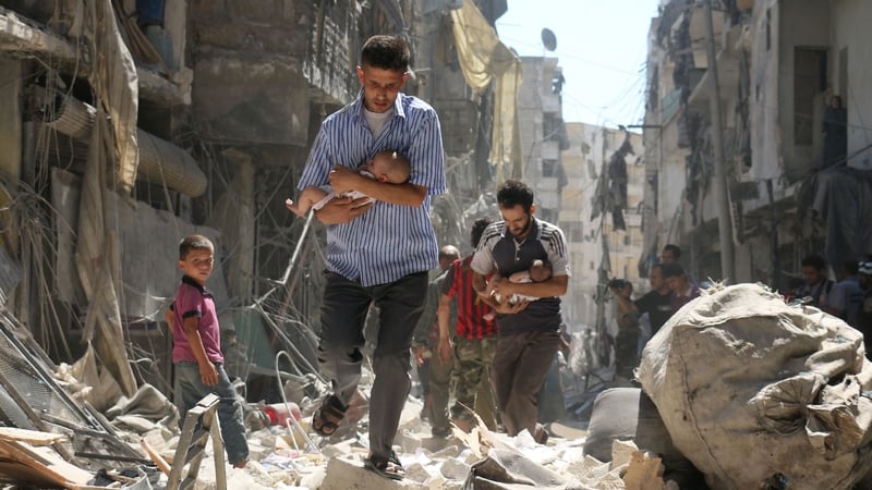 Syrian men carrying babies make their way through the rubble after an air strike in Aleppo in September 2016