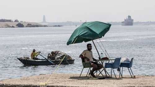 A fisherman takes a rest as a cargo ship sails through the Suez Canal in 2019