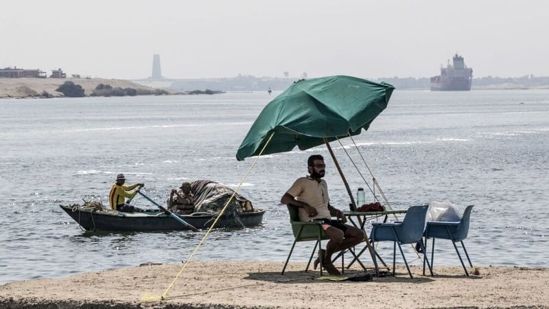 A fisherman takes a rest as a cargo ship sails through the Suez Canal in 2019