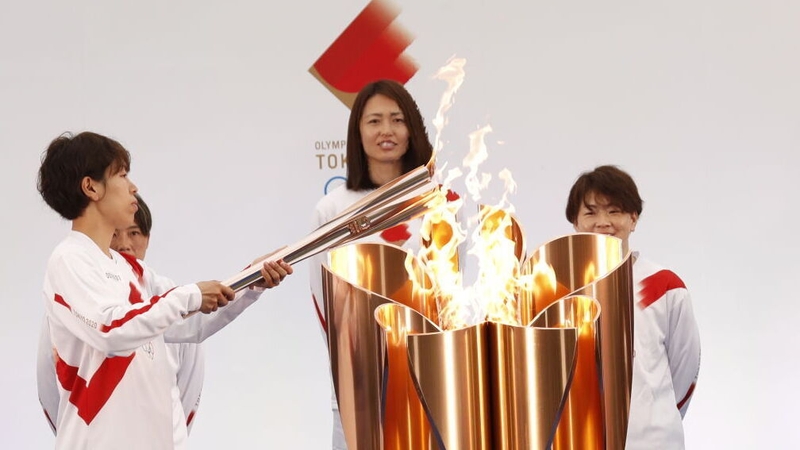 Azusa Iwashimizu (L), a member of Japan women's football national team, lights the torch from the celebration cauldron in Fukushima