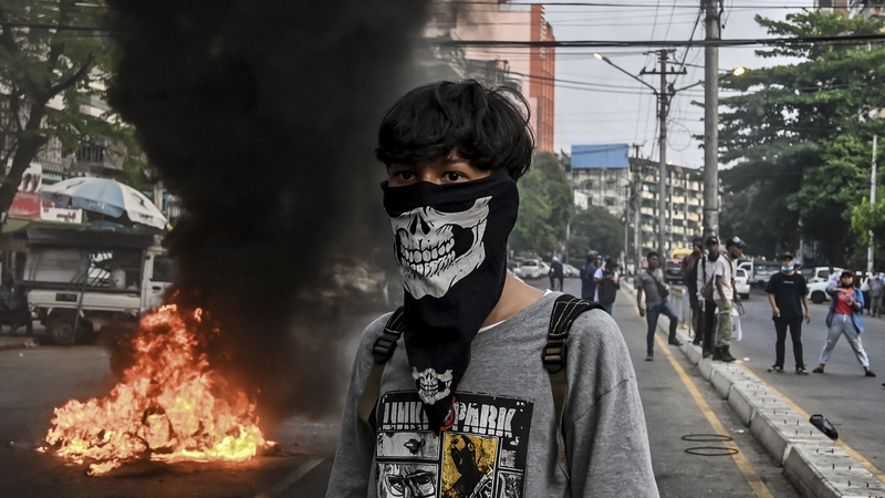 A protester stands near a burning makeshift barricade in Yangon