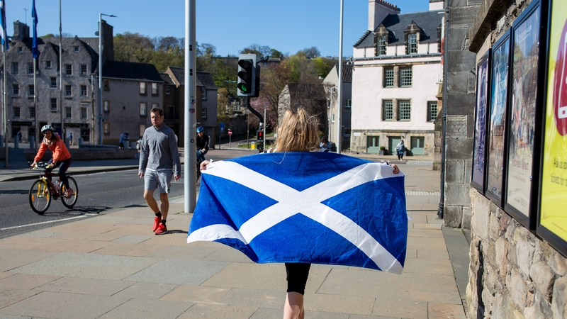 A woma walks with her towel featuring the saltire design of the national flag of Scotland outside the Scottish Parliament at Holyrood, Edinburgh, U.K.