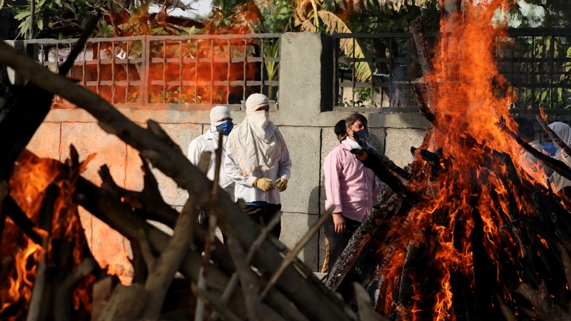 Family members stand behind the funeral pyres as they attend the last rites for victims at a cremation ground in New Delhi