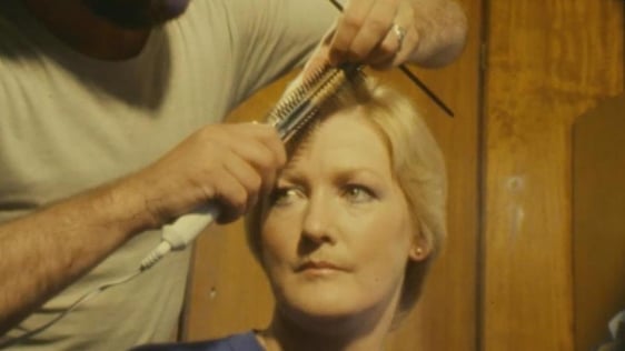 Hairdresser styling woman's hair using a hot curler brush (1981)