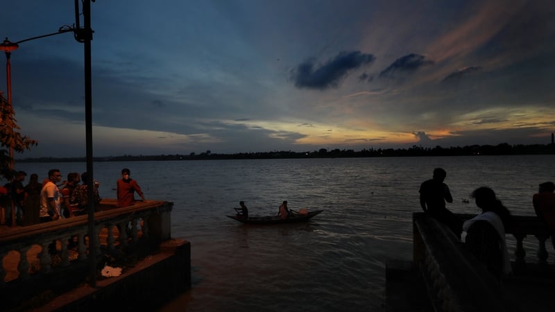 Locals wear face protective masks as they stand on the bank of river Ganges during sunset in Kolkata