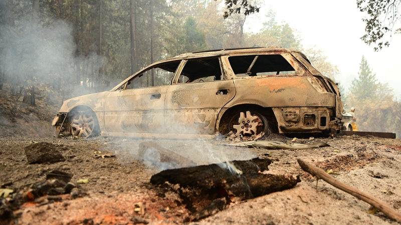 A log smoulders in front of a burnt car at Shasta Lake, California