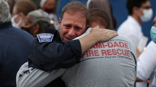 Rescue workers with the Miami Dade Fire Rescue embrace near the memorial site for victims
