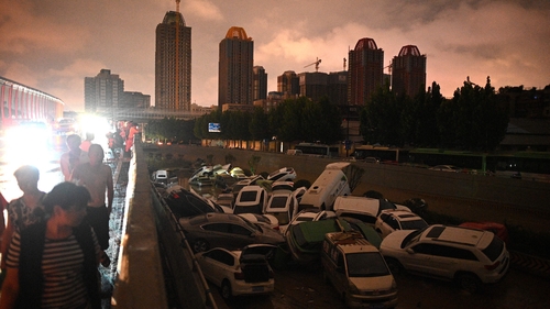 People look at cars stacked on each other at an entrance of a tunnel following the heavy rains