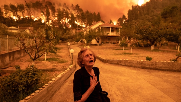 An elderly resident reacts as a wildfire approaches her house in the village of Gouves, on the island of Evia