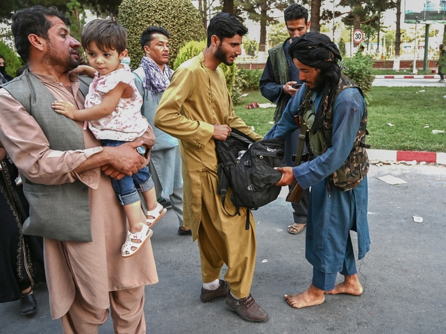 A Taliban fighter (right) searches the bags of people coming out of the Kabul airport