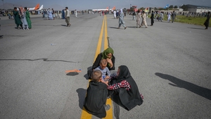Afghan people sit along the tarmac as they wait to leave the Kabul airport