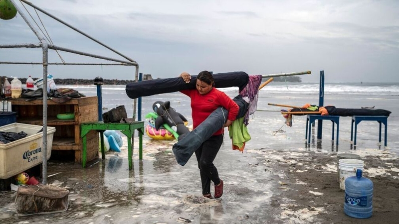 A woman removes umbrellas from the beach as strong waves reach the coast in Veracruz