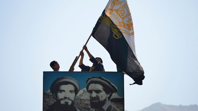 Afghan men wave a flag above the portrait of late Afghan commander Ahmad Shah Massoud