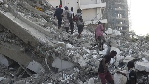 People walk to rescue workers from the rubble of a 21-storey building under construction that collapsed in Lagos
