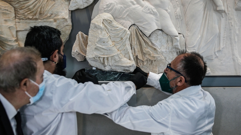 Acropolis museum staff members display the marble fragment from the Parthenon