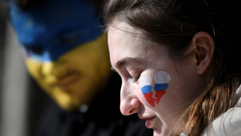 A man with the Ukrainian colours on his face, and a woman with a broken heart in the colours of the Russian flag at a protest in France